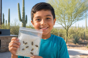 A smiling boy in a blue T-shirt looks at the camera and holds up a clear pouch of sprouting sunflower seeds, with saguaro cacti and desert trees behind him