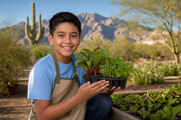 A smiling boy in a blue shirt and light brown apron holds up a tray of seedlings in a backyard garden, with a large saguaro, desert trees and distant mountains behind him