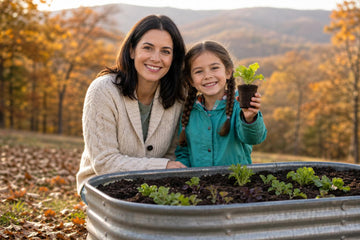 A smiling mother in a cream sweater and her young daughter in a blue jacket face the camera beside a metal raised garden bed, the girl holding up a small potted seedling, with autumn trees behind them