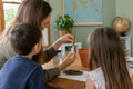 A parent and two children at a homeschool table dipping a bare, leafless avocado tree cutting into rooting powder