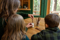 A parent and two children at a cabin table dipping a bare, leafless redwood tree cutting into rooting powder